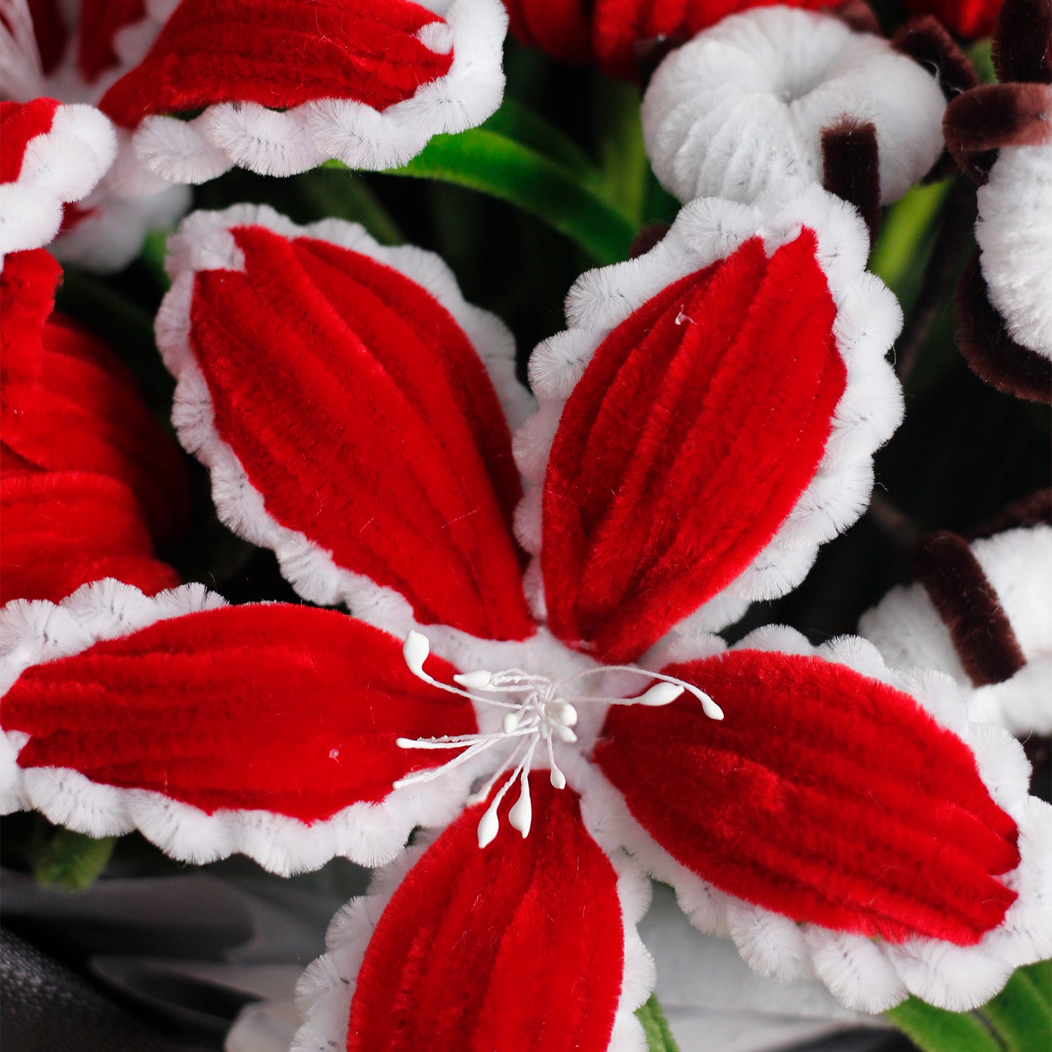 Red and white handmade pipe cleaner bouquet wrapped in festive Christmas paper with red bow. Features poinsettia-inspired flowers and snowflake accents. Ideal for holiday gifts.
