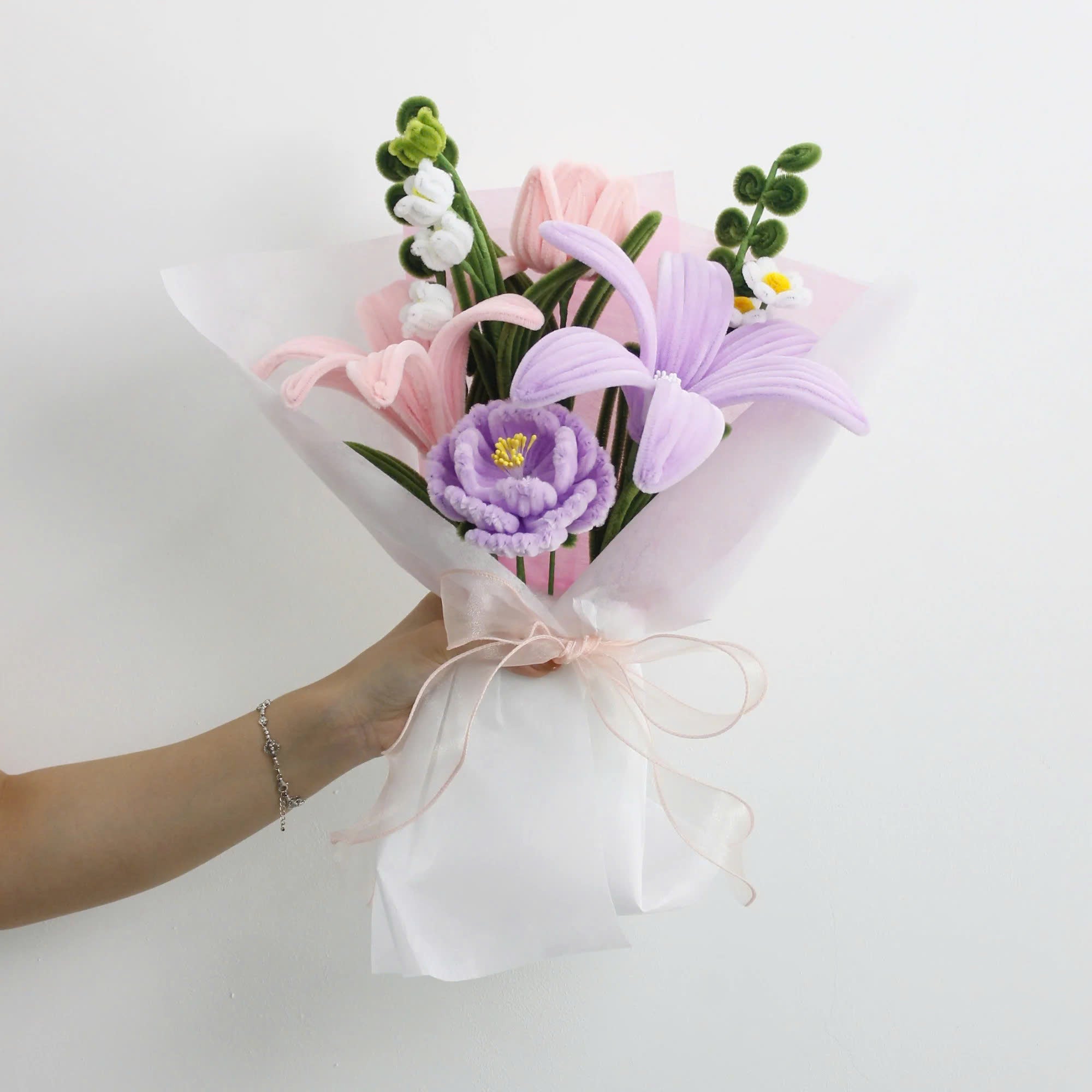 Lily Whisper DIY bouquet made from soft pipe cleaners, featuring pastel lilies, tulips, and a blooming purple carnation. Wrapped in sheer white and pink layers with a soft organza bow a handmade floral gift full of grace.