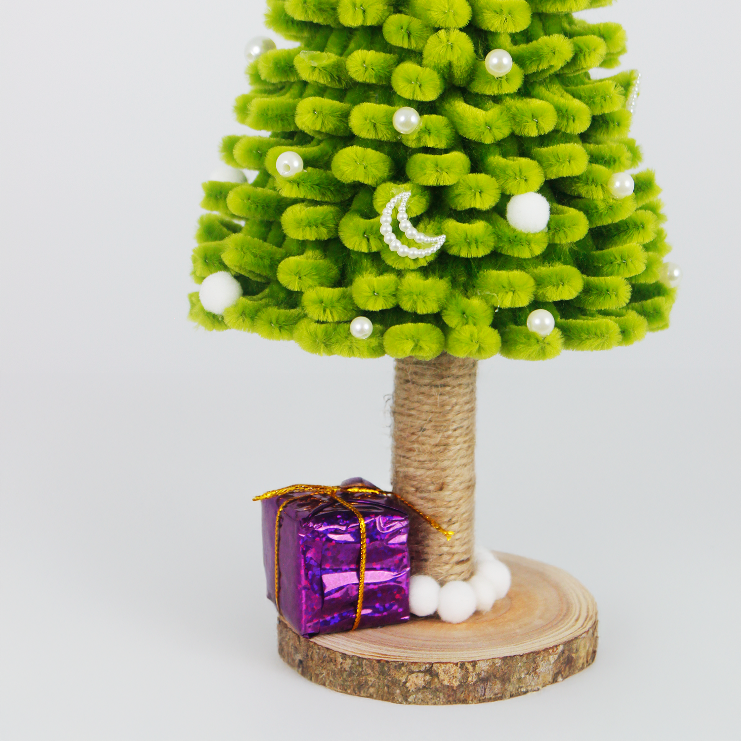 Green fuzzy pipe cleaner Christmas tree with white pom-poms and purple gift box. Cute handmade décor for holiday season.