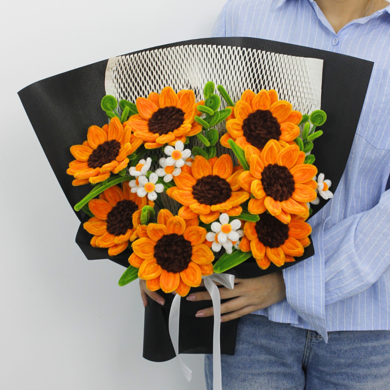 Person holding a bouquet of orange sunflowers and white flowers against a white background