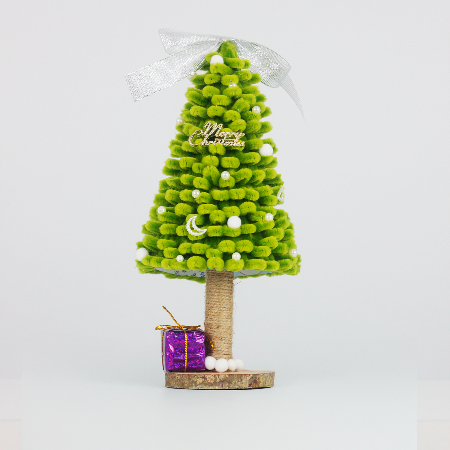 Green fuzzy pipe cleaner Christmas tree with white pom-poms and purple gift box. Cute handmade décor for holiday season.