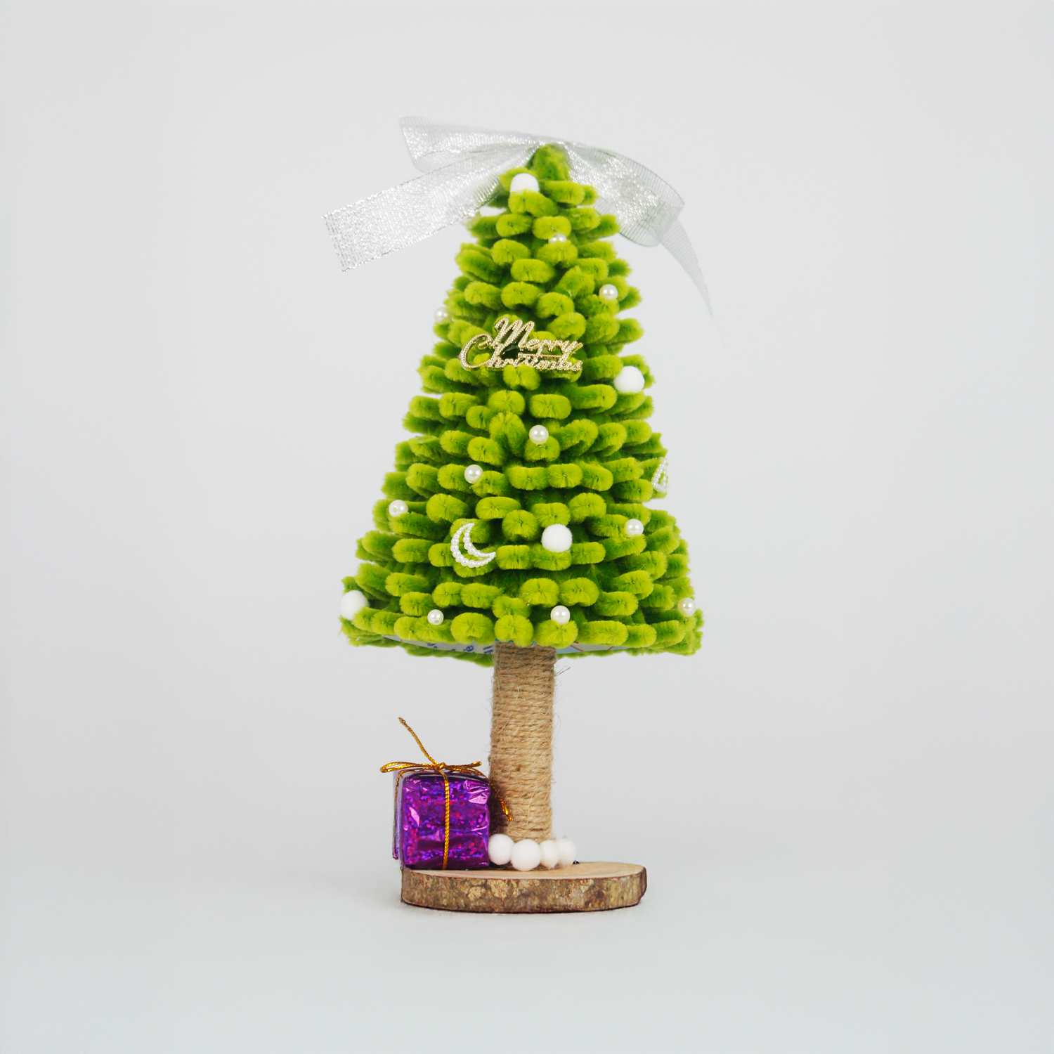 Green fuzzy pipe cleaner Christmas tree with white pom-poms and purple gift box. Cute handmade décor for holiday season.