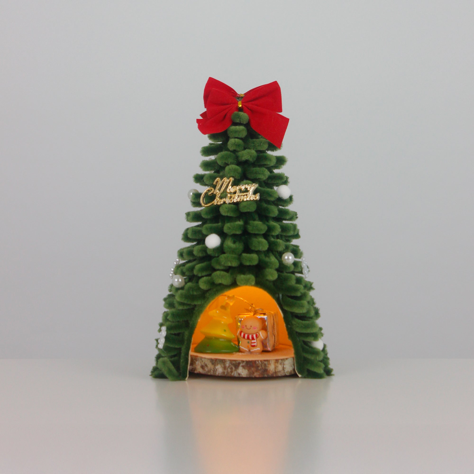 Unique handmade Christmas tree cabin crafted from green pipe cleaners, with lights and gingerbread decor – cozy holiday display.