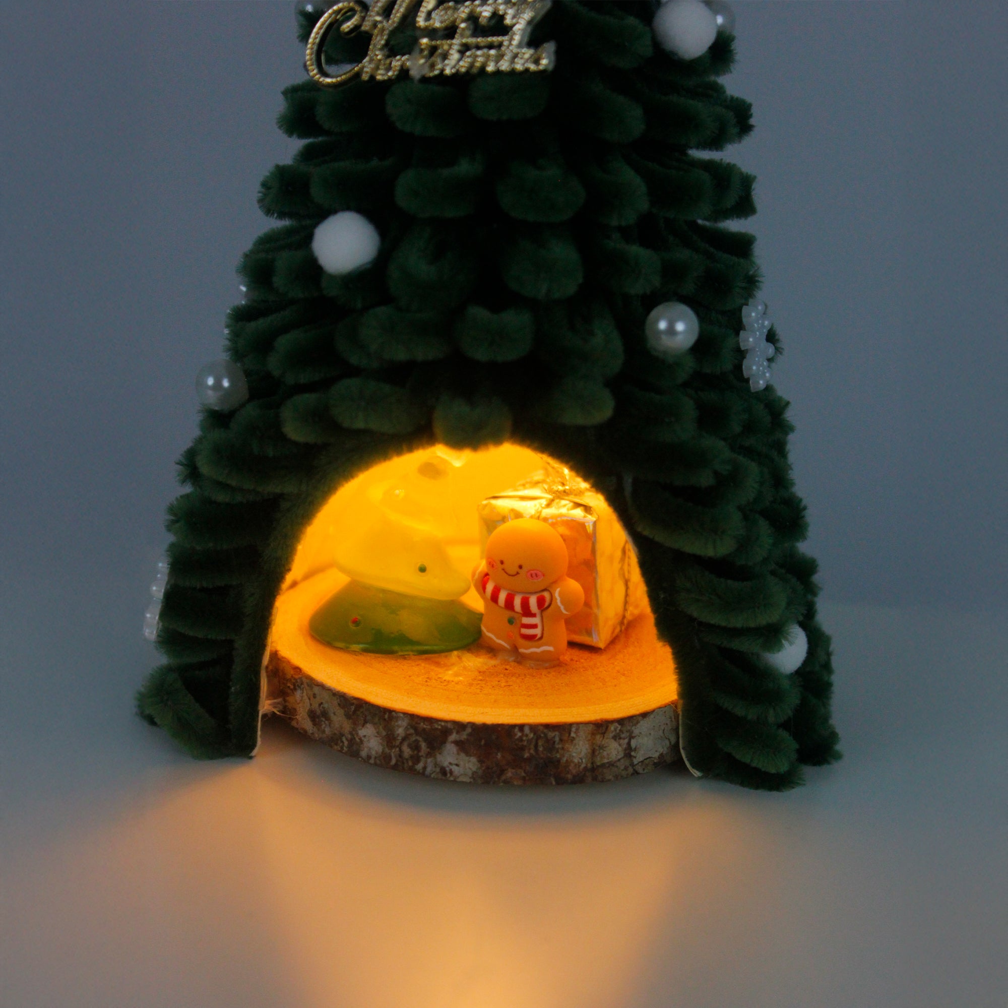 Unique handmade Christmas tree cabin crafted from green pipe cleaners, with lights and gingerbread decor – cozy holiday display.