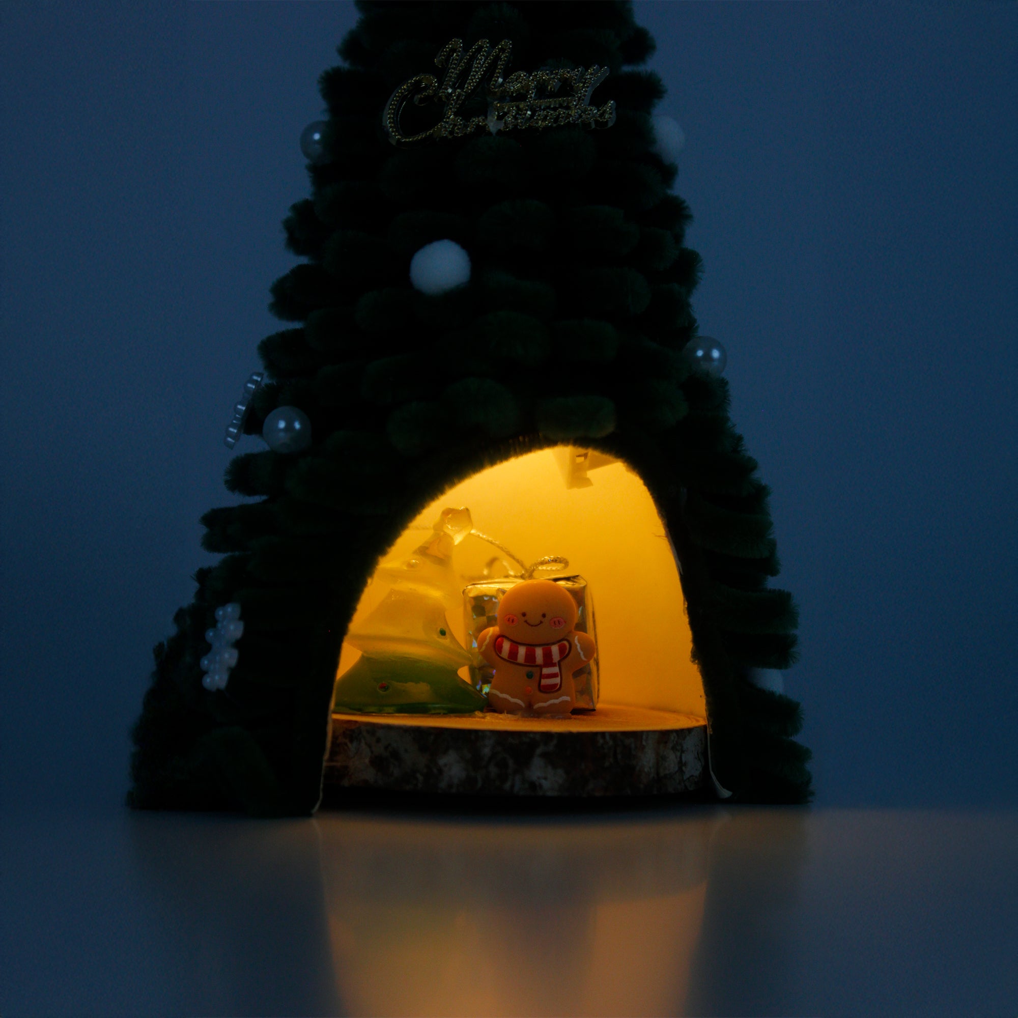 Unique handmade Christmas tree cabin crafted from green pipe cleaners, with lights and gingerbread decor – cozy holiday display.