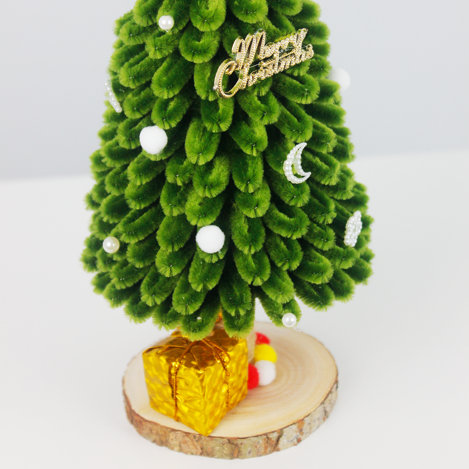 Green pipe cleaner Christmas tree with silver ribbon, mini ornaments, pom-poms, and golden gift box on rustic wood base – perfect handmade holiday decor or DIY Christmas gift