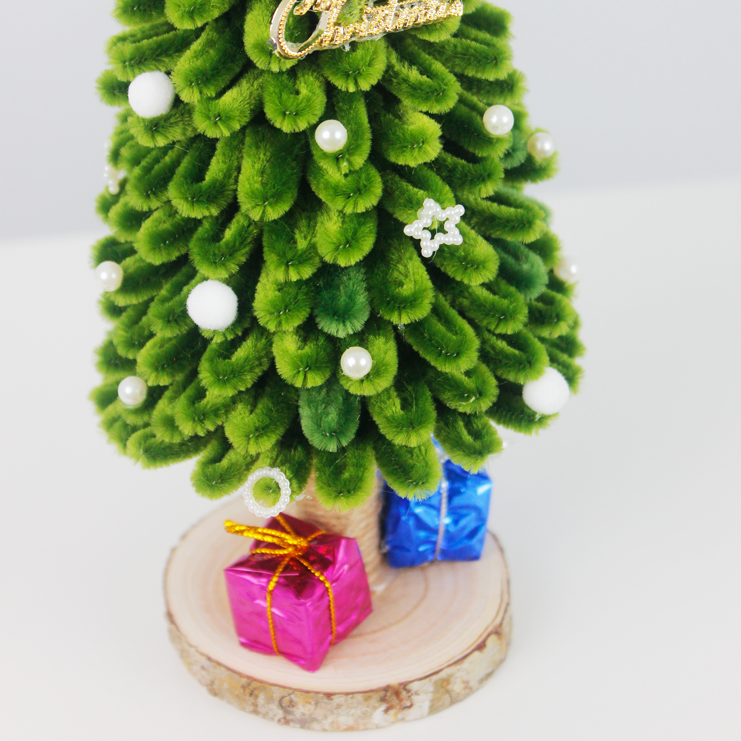 Handmade green pipe cleaner Christmas tree decorated with white pearls, silver bow, and "Merry Christmas" sign, displayed with pink and blue gift boxes on a wooden base — perfect for festive decor or gift.